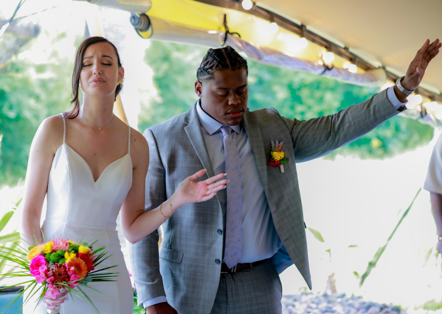 Marina and Anthony side by side with eyes closed and hands raised during the ceremony